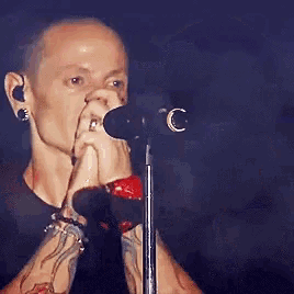 a man is singing into a microphone with his hands on his face .