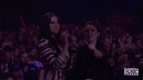 a woman is singing into a microphone in front of a crowd of people at an american music awards show .