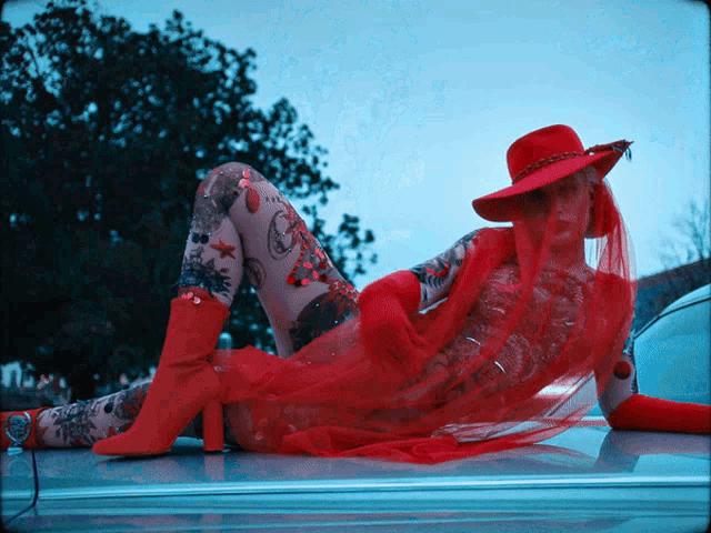 a woman laying on the hood of a car wearing a red hat