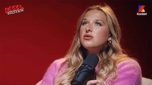 a woman in a pink sweater is sitting in front of a microphone with the words love interview on the bottom