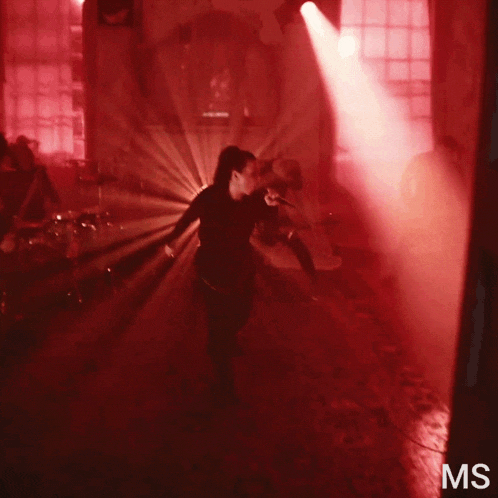 a woman singing into a microphone in a dark room with the letters ms visible