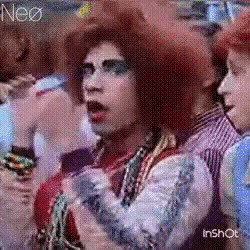 a woman with red hair is sitting in a crowd of people and making a funny face .