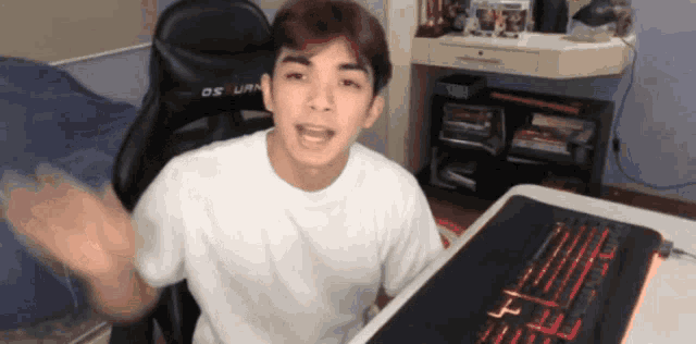 a young man is sitting at a desk with a keyboard and a chair that says os uran on it