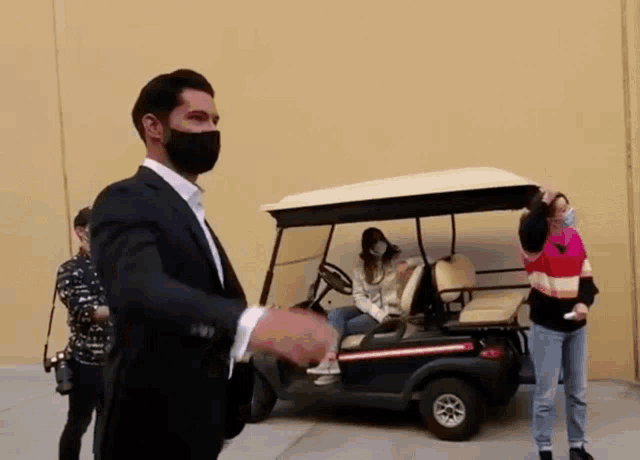 a man wearing a black mask stands next to a golf cart