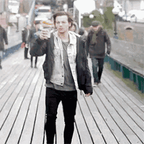 a man in a denim jacket is walking down a wooden boardwalk holding a cup of coffee .