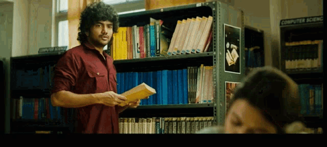 a man in a red shirt is holding a book in front of a computer room
