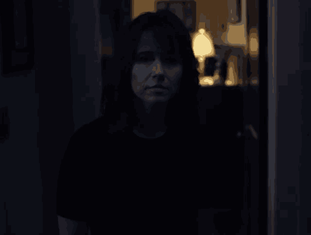 a woman in a dark room with a lamp in the background
