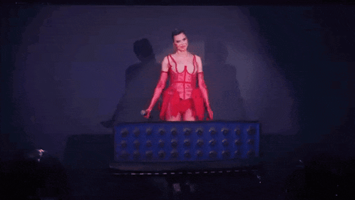 a woman in a red dress and red gloves is standing on a stage in front of a blue box .