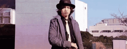 a man wearing a hat , coat and tie is standing in front of a building .