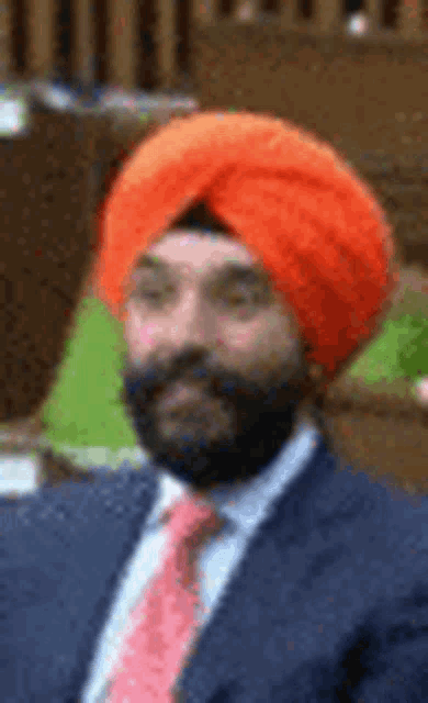a man with a beard wearing an orange turban and a suit .