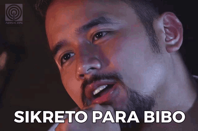a man with a beard says " sikreto para bibo " in a dark room