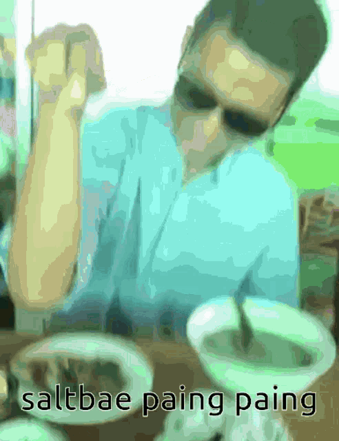 a blurry picture of a man sitting at a table with the words saltbae paing paing written below him