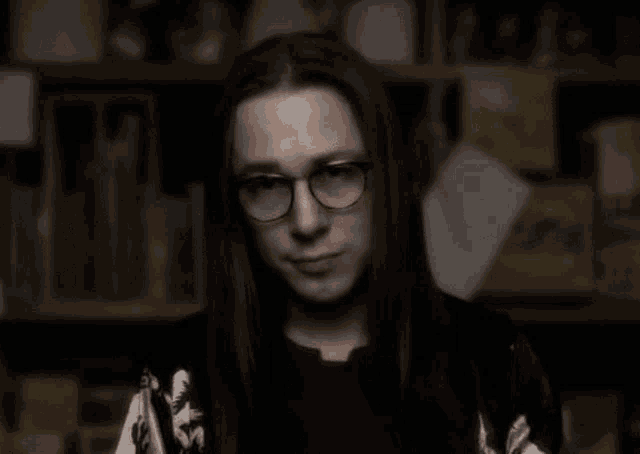 a man with long black hair and glasses is looking at the camera .