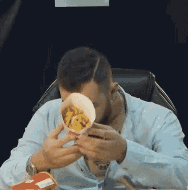 a man is sitting at a table eating french fries from a paper cup .