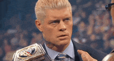 a man in a suit and tie is holding a wrestling championship belt and talking to another man .