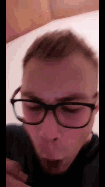 a man wearing glasses and a black shirt is laying on a bed