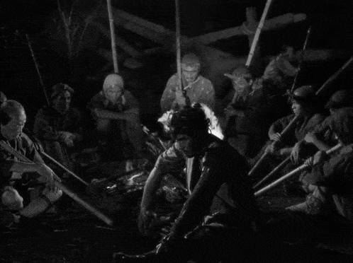 a black and white photo of a group of people sitting around a campfire