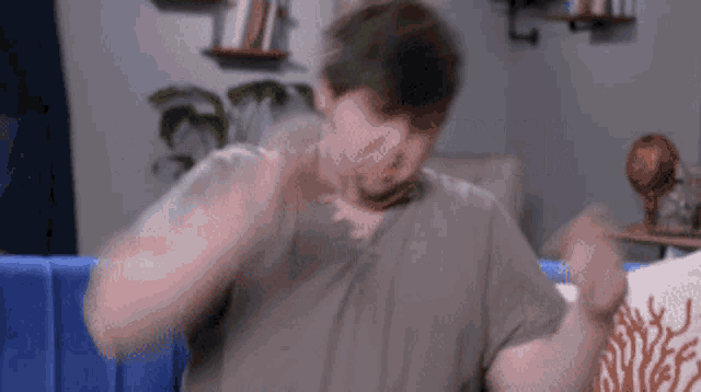 a man in a grey shirt is sitting on a blue couch making a funny face .