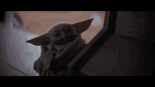a baby yoda is sitting on a staircase looking out of a window .
