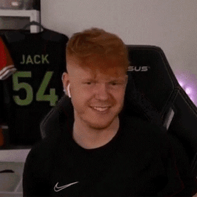 a young man with red hair and a beard is sitting in a chair and smiling .