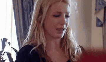 a blonde woman is sitting in a living room with her eyes closed and her mouth open .