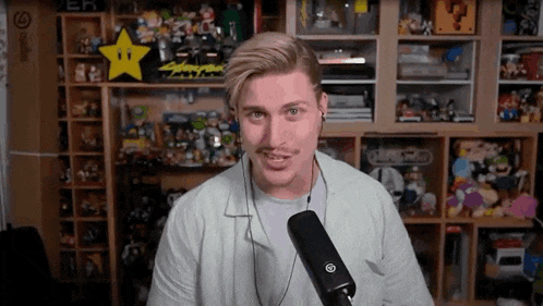 a man with a mustache is talking into a microphone in a room filled with lots of toys .