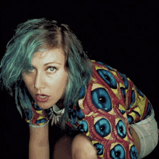 a woman with green hair is wearing a colorful shirt with circles on it