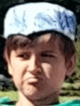 a young boy wearing a white hat and a green shirt is making a face .