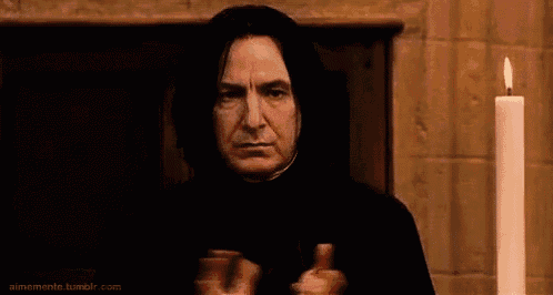a man in a black robe is giving a thumbs up in front of a fireplace and a candle .
