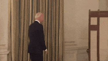 a man in a suit and tie is walking through a room with curtains .