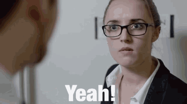 a woman wearing glasses and a suit is talking to a man and says yeah !