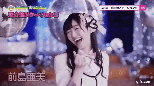 a girl with a flower in her hair is smiling and making a heart shape with her hands