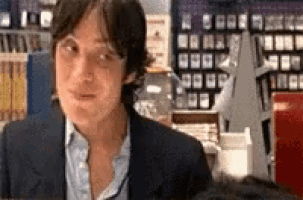 a man in a suit and blue shirt is sitting in front of a bookshelf .