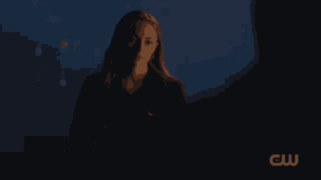 a woman in a dark room with a cw logo on the bottom right