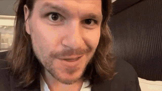 a man with long hair and a beard is looking at the camera and making a funny face .