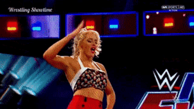 a woman is dancing on a stage with a wrestling logo in the background .