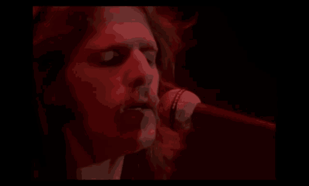 a man is singing into a microphone in a dark room in front of a red light .
