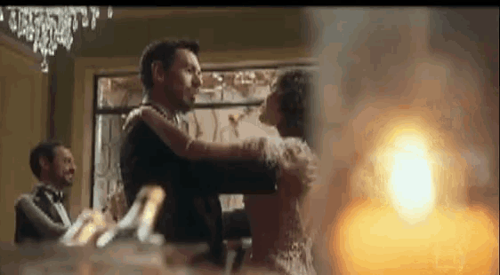 a man in a tuxedo is holding a woman in his arms while they dance in a room .