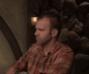 a man in a plaid shirt is sitting in front of a stone wall and looking at something .