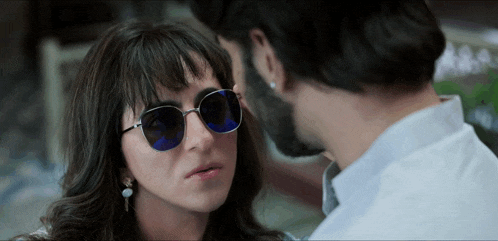 a woman wearing sunglasses looks at a man