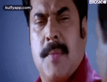 a man with a mustache and a red shirt is making a funny face with his eyes closed .
