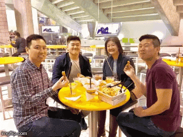 a group of people are sitting around a yellow table eating food and drinking