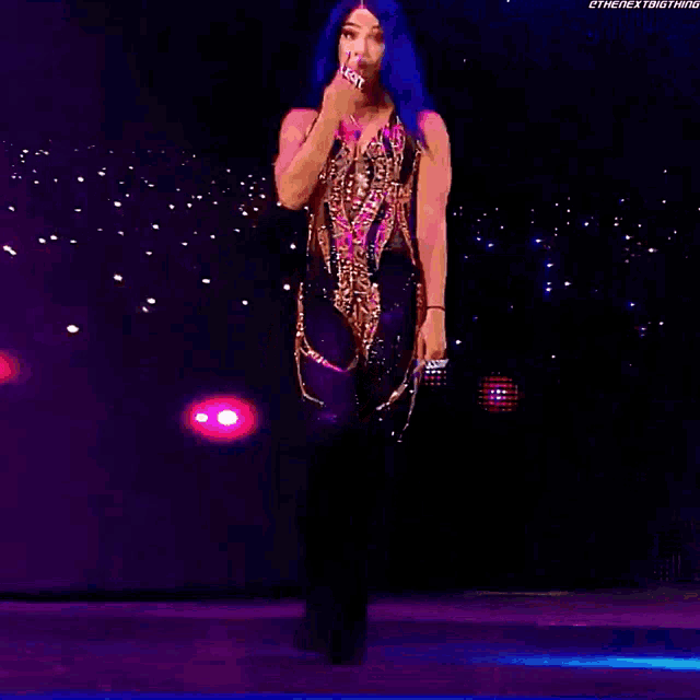 a woman with blue hair is standing on a stage in front of a purple background .