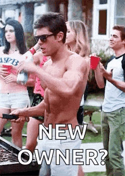 a shirtless man is cooking food on a grill with a group of people standing around him .