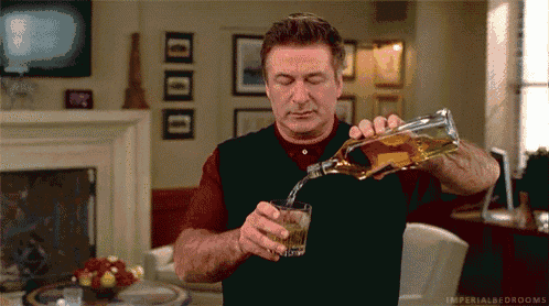 a man is pouring a glass of whiskey from a bottle in a living room