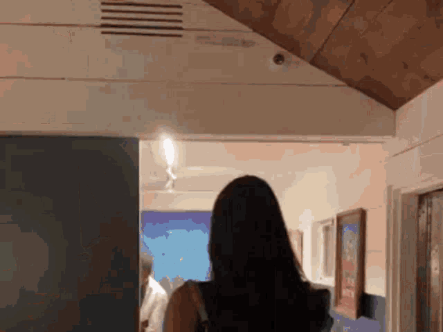 a woman is walking through a hallway with a wooden ceiling and a painting on the wall .