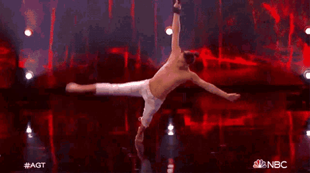 a man without a shirt is doing a trick on a stage with a nbc logo in the background