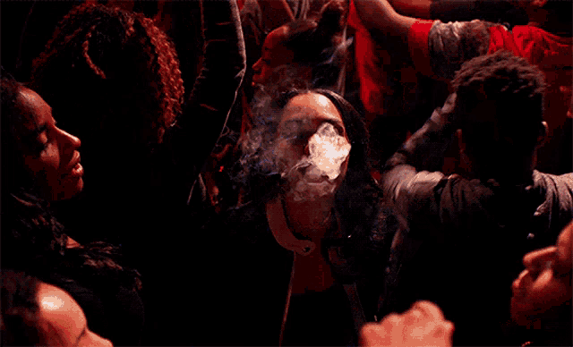 a woman is smoking a cigarette in a crowd at a party