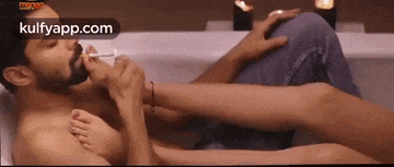 a man is smoking a cigarette while laying in a bathtub with a woman 's feet on his lap .