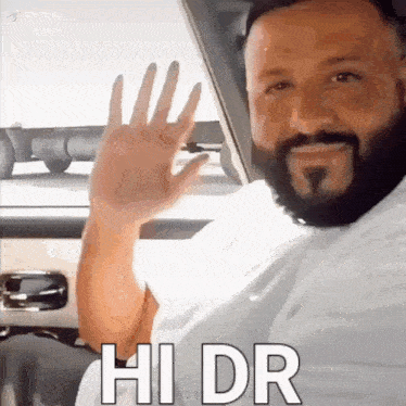 a man with a beard is sitting in a car waving his hand and says hi dr .